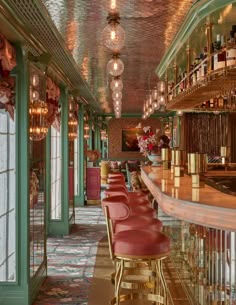 a long bar with red leather chairs and gold trim around the bar area, along with chandeliers hanging from the ceiling