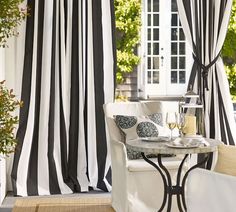 black and white striped curtains in front of a patio table with two glasses of wine on it