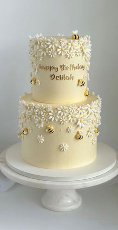 a three tiered cake decorated with daisies and bees