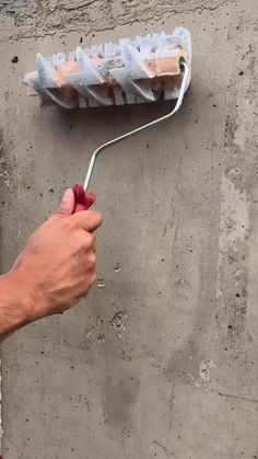 a person holding a paint roller in their hand next to a cement wall with plaster on it