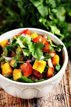 a white bowl filled with chopped vegetables and cilantro on top of a wooden table