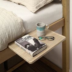 a book, coffee mug and eyeglasses are on a small table next to a bed