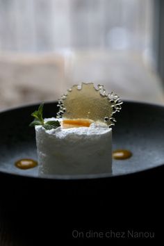 a small piece of food sitting on top of a black plate next to a window