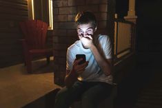 a young man sitting on a porch holding a cell phone in his hand and looking at the camera