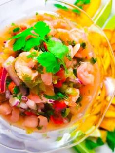 a bowl filled with shrimp and vegetables on top of a white table next to green leaves