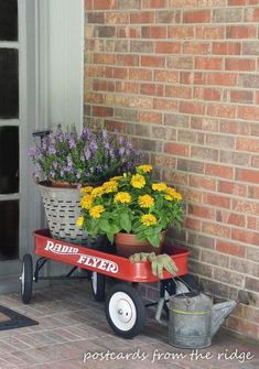 a red wagon filled with flowers sitting on top of a brick floor next to a door