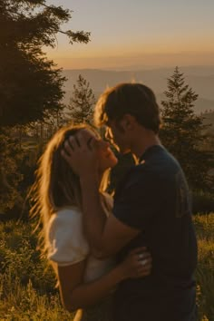 a man and woman are kissing in the woods at sunset with mountains in the background