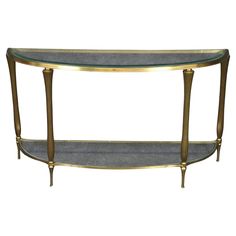 an oval glass and brass console table with two shelves on each side, against a white background