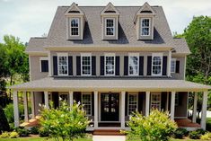 a house with black shutters and white trim on the front porch, surrounded by greenery