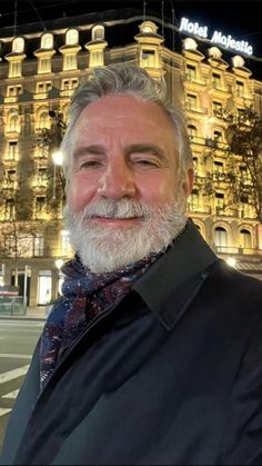 a man with grey hair and beard standing in front of a large building at night