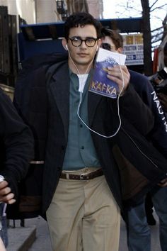 a man walking down the street with headphones in his ears and holding a book