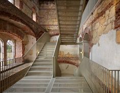 there is a very long stair case in the building with stone walls and brick floors