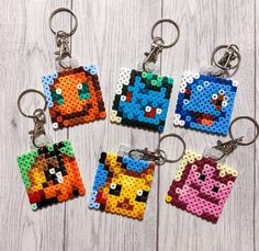 four pixel keychains are shown on a white wooden surface, each with an image of the same character