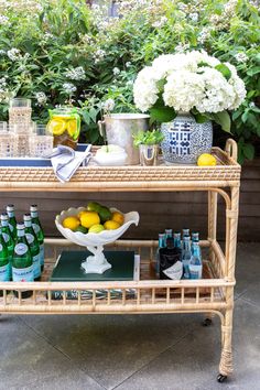 a wicker bar cart with lemons and bottles on it in front of flowers