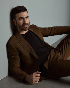 a man sitting on top of a cement floor next to a wall wearing a brown suit and black t - shirt