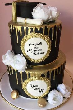 two tiered black and gold wedding cake with white flowers on the side, covered in chocolate icing