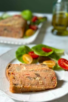 two pieces of bread sitting on top of a white plate next to salad and olives