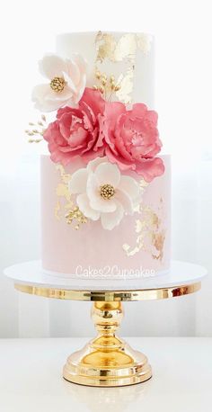 a pink and gold wedding cake with large flowers on the top, sitting on a white table