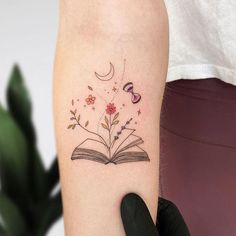 a woman's arm with a book and flowers tattoo on the left side of her arm