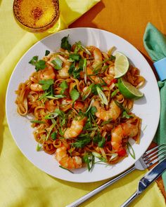 a white plate topped with pasta and shrimp next to a glass of orange juice on a yellow table cloth