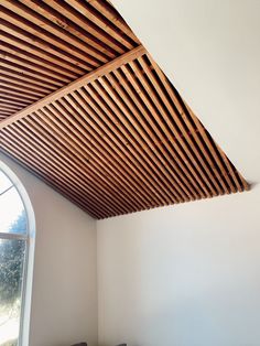 a room with a window and wooden slatted ceiling above the bed, in front of an arched window