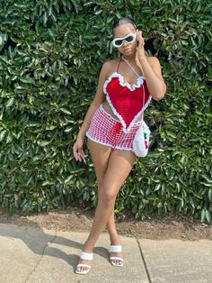 a woman in a red and white bathing suit talking on a cell phone while standing next to a bush