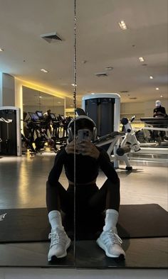 a woman taking a selfie in front of a mirror at a gym with her cell phone