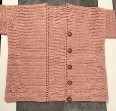 a pink knitted sweater sitting on top of a white table next to a gray wall