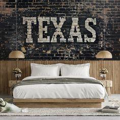 a bed with white sheets and pillows in front of a brick wall that says texas