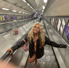 a woman is standing on an escalator with her arms spread out and looking at the camera