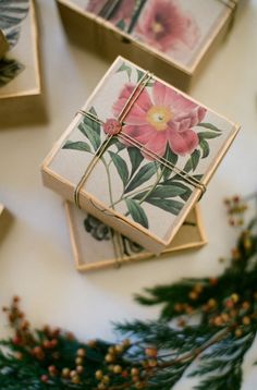 four square coasters decorated with pink flowers and green leaves on a white tablecloth