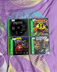 three video games sitting on top of a purple bed sheet next to an orange and black object