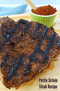 a piece of steak sitting on top of a cutting board next to a bowl of spices