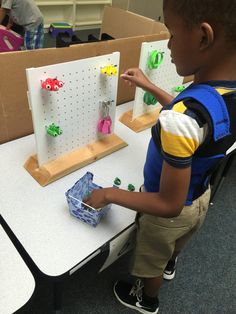 a young boy standing in front of a table with pegboards and magnets on it