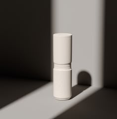 a small white bottle sitting on top of a table next to a shadowless wall