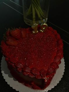 a heart shaped cake sitting on top of a table next to a vase with strawberries