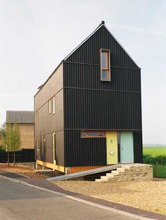 a black house sitting on the side of a road next to a lush green field