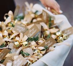 a bunch of gold and white christmas bells in a box with ribbon around them, being held by a woman's hand