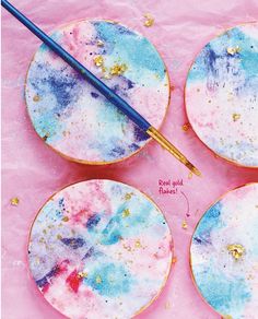 four painted plates with paintbrushes sitting on top of each other next to pink paper