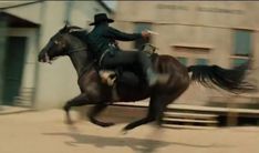 a man riding on the back of a brown horse next to a wooden bench in front of a building