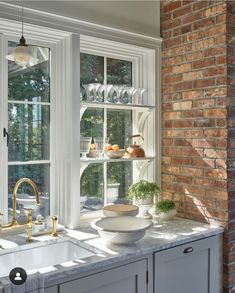 a kitchen sink sitting under a window next to a brick wall