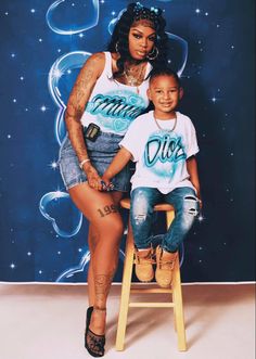 a woman sitting on top of a wooden stool next to a little boy in front of a blue background