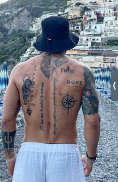 a man with many tattoos on his back standing in front of the ocean and buildings