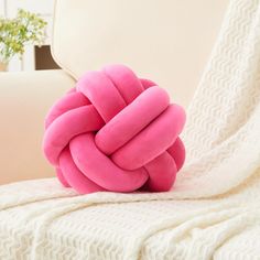 a pink knot pillow sitting on top of a white couch next to a plant in a vase