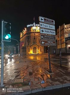 street signs in front of a building on a wet city street at night with traffic lights