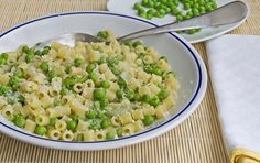 a bowl filled with pasta and peas on top of a table next to two plates