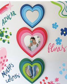 three heart shaped mirrors hanging on a wall with flowers and hearts in the middle, one is holding a cell phone