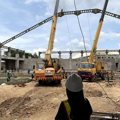 some construction workers are standing in front of two large cranes and one is working on the ground