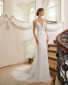 a woman in a white wedding dress standing on some stairs near a mirror and railing