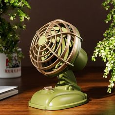 a desk fan sitting on top of a wooden table next to a laptop and potted plant